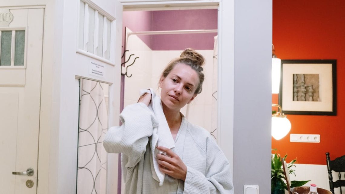 A woman in a bathrobe drying off after a shower in a cozy home bathroom.